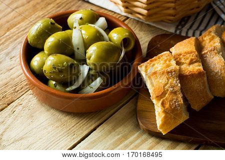 Jumbo gordal olives with herbs and onions rustic baguette on wood background