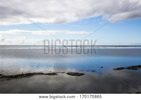 shoreline of Ameland Island with view over the wadden sea with clouds and tourmented sky reflecting in water at dawn