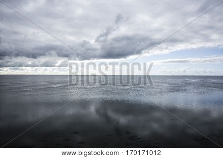 shoreline of Ameland Island with view over the wadden sea with clouds and tourmented sky reflecting in water at dawn