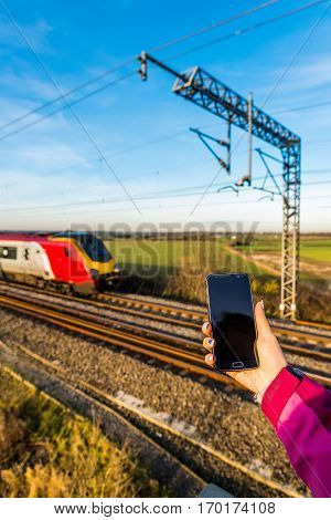 Day View Of Woman Hand Holding Smartphone Over Uk Railroad.