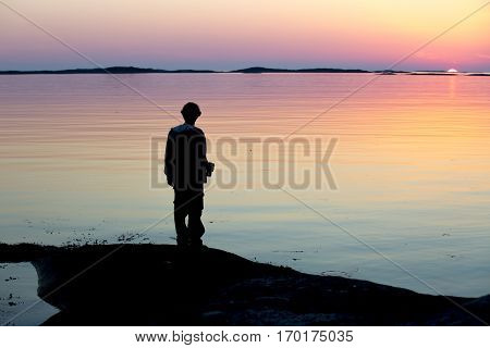Norwegian landscape in the midnight sun with a silhouette of a man admiring the landscape