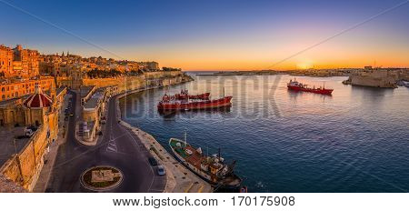 Valletta Malta - Panoramic shot of an amazing summer sunrise at Valletta's Grand Harbor with ships and the ancient houses and walls of the maltese capital city.