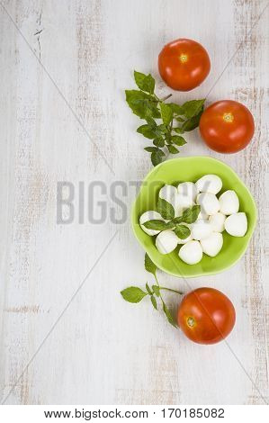 Mozzarella in a green plate on a wooden table. Mozzarella balls with basil leaves and tomato on a wooden board. Ingredients for caprese salad.