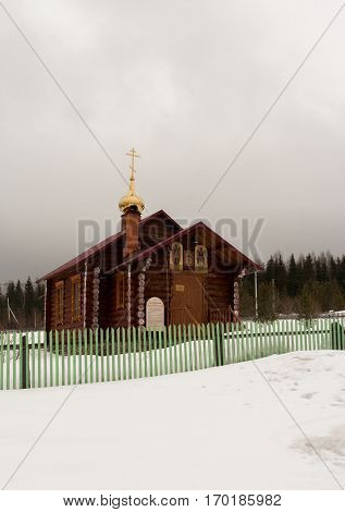 Verkhniy Tagil, Russia - 11.07.2016: Small wooden Church standing in snow behind green fence near forest.