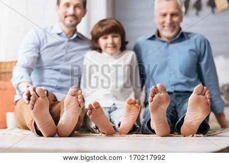 Male members of the family. Happy positive delighted members of the family sitting on the floor and showing their feet while spending time together