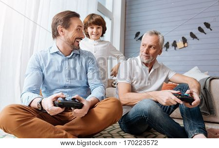 Modern entertainment. Happy delighted bearded man holding a game console and looking at his father while playing computer games with him