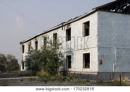 Burnеd light blue two-storeyed building with green trees. After fire