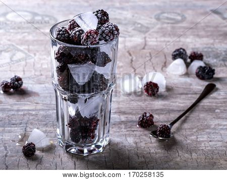Glass tumbler with blackberries and ice on a gray background. Spoon the berries next