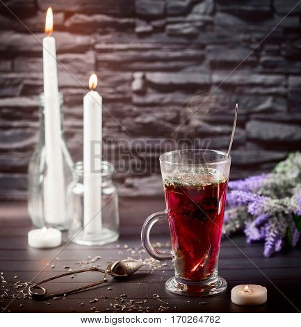 Hibiscus tea in glass Cup. The candles in the background. Tea strainer nearby. Dark background. Selective focus