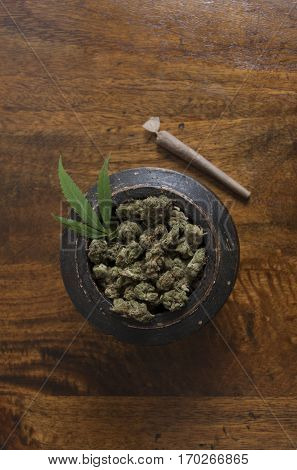 Cannabis sativa flower buds and leaf in wooden pot with rolled weed joint