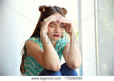 Sad teenage girl sitting near window