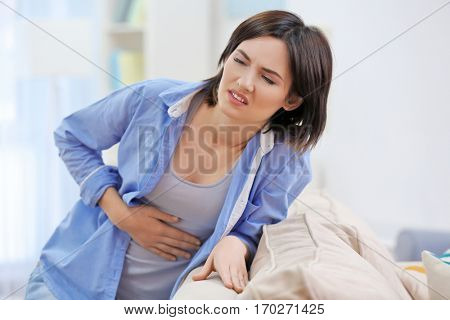 Beautiful young woman suffering from stomach ache at home