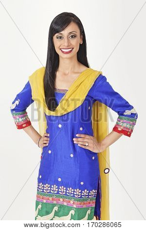 Portrait of pretty Indian woman in traditional wear standing with hands on hips over gray background