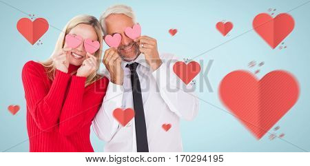 Silly couple holding hearts over their eyes against blue background