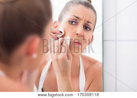Woman popping pimples in front of bathroom mirror