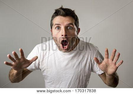 young attractive man astonished and amazed in shock and surprise face expression as paradigm of facial for shock emotion isolated on grey background