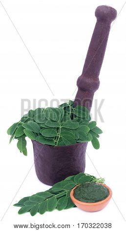 Edible moringa leaves in a vintage mortar with ground paste over white background