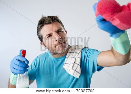 portrait of domestic service man or busy husband concentrated doing house cleaning with spray bottle and sponge washing glass carefully pointing the camera isolated even background