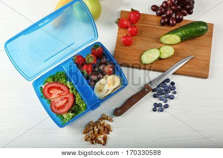 Lunchbox with sandwich and fruits on white wooden table