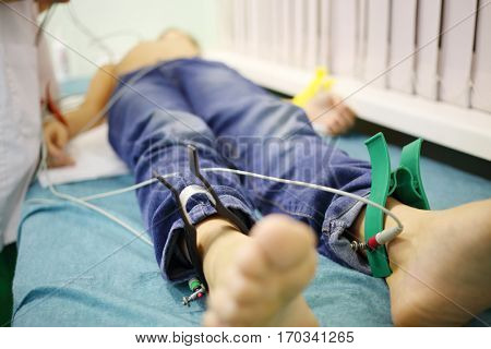 Nurse adjusts probes on young patient which lies on bed in hospital, focus on the electrodes