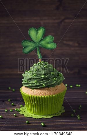 Cupcake with clover cakepick on a wooden background