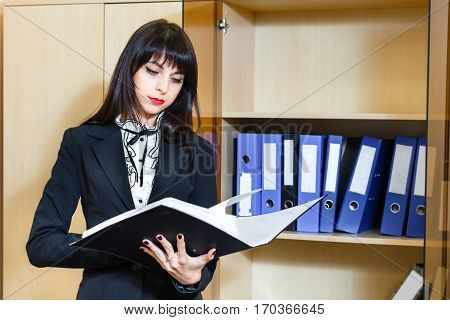 Beautiful young brunette woman reading a documents in office.