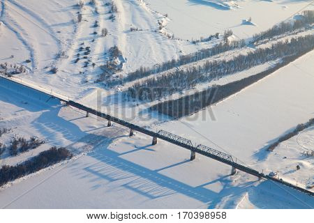 Aerial view of snow covered winter landscape of river valley and train, which crossing river on bridge
