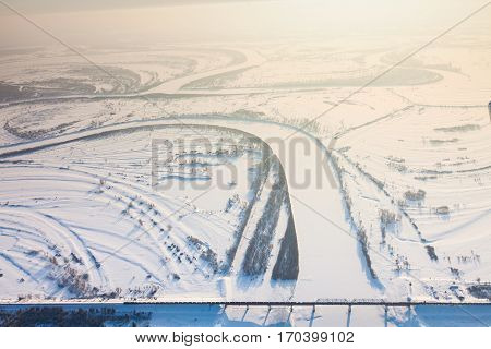 Aerial view of snow covered winter landscape of river valley and train, which crossing river on bridge