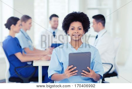 clinic, profession, people and medicine concept - happy female doctor or nurse with tablet pc computer over group of medics meeting at hospital