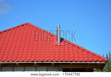 New red metal tiled roof with steel chimney house roofing construction exterior without rain gutter system.