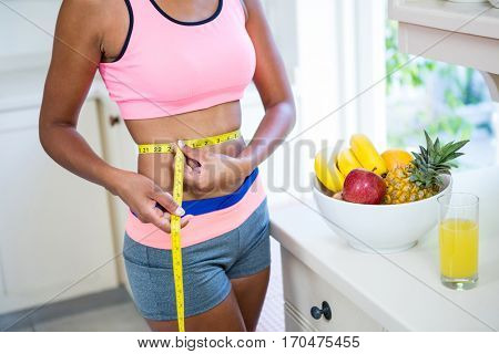 Mid-section of woman measuring her waist at home