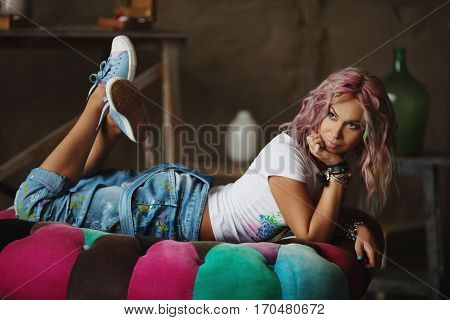 The artist with multi-colored hair in paint-stained jeans, lying on his stomach