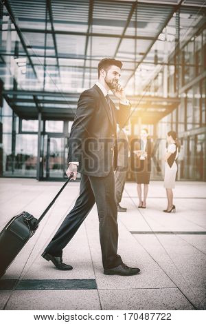 Businessman holding suitcase talking on mobile phone in office premises