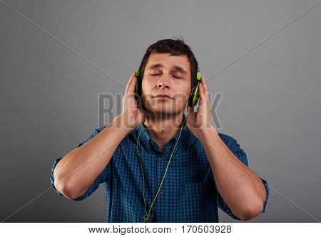 Handsome guy listen relax music with closed eyes. DJ keep headphones by two hands. Emotion portrait of relaxing man in sudio with neutral grey background.