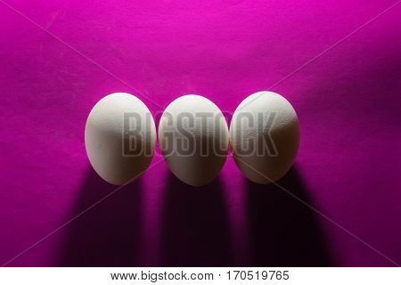 White close up three eggs isolated on purple paper textured background. minimalism concept