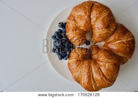 Three tasty croissants and blue blueberry on the white plate on the white table