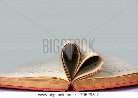 Open book pages curved into heart symbol and grey empty background