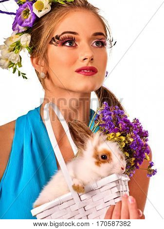 Easter girl holding bunny and eggs. Woman with holiday spring flowers hairstyle and make up holding rabbit in basket . White background. Makeup with fake eyelashes.