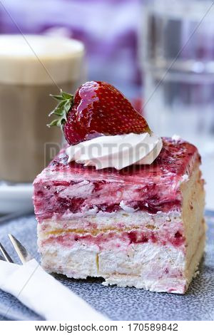 Strawberry sponge cake with cream, with latte coffee behind.  Outdoor setting, focus on strawberry.