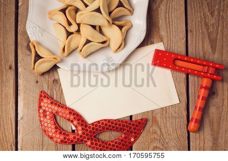 Purim holiday concept with greeting card hamantaschen cookies and carnival mask on wooden background. Top view from above