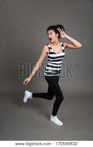 Full length of scared african american young woman running away over grey background