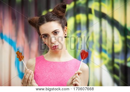 Young girl in a pink dress with candy on a decorated background of graffiti wall