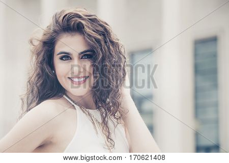 Feminine beauty. Curly hair young smiling woman. A young, smiling and attractive woman with makeup. She has long curly hair. Sensual and radiant beauty.