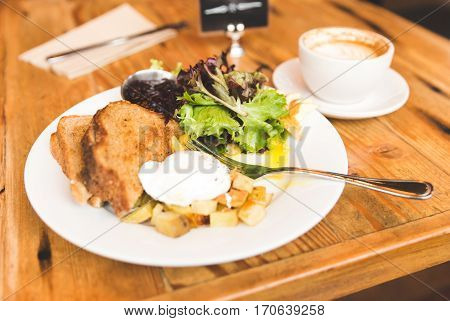 Eggs potatoes lettuce toast and coffee in a breakfast meal spread. Upscale cafe setting.