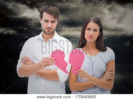 Composite image of depressed couple holding broken heart against storm clouds