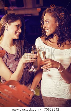 Cheerful young women toasting champagne flutes at bar counter against love heart pattern