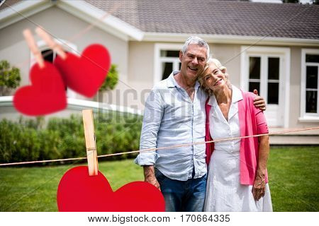 Portrait of smiling senior couple embracing each other against hearts hanging on line
