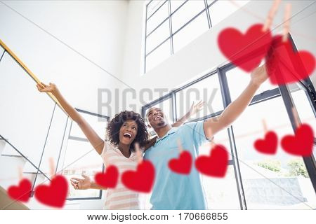 Composite image of couple embracing at home with hanging hearts around