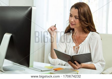 Happy businesswoman holding notepad at desk in office