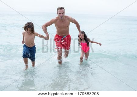 Happy father running with children at beach against sky